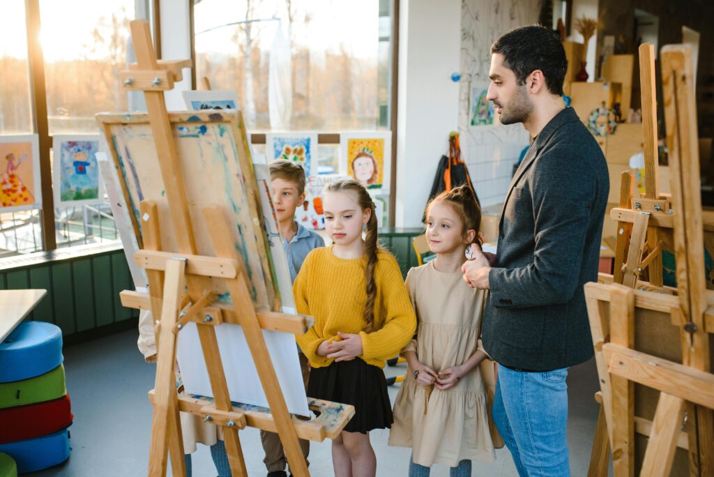 Children engaged in an art class under teacher's guidance, painting on easels.